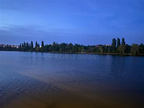 Night Landscape View Of Blue Lake With Trees And Blue Sky Reflecting On