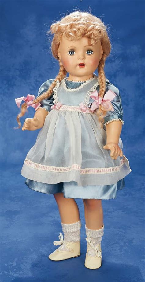 a doll with blonde hair wearing a blue dress and white shoes holding a pink flower in her hand