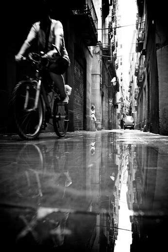a man riding a bike down a street next to tall buildings on either side of a puddle
