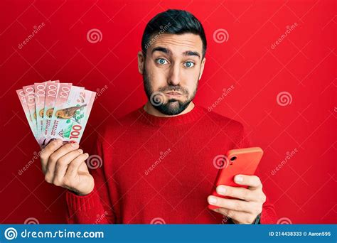 Young Hispanic Man Using Smartphone Holding New Zealand Dollars