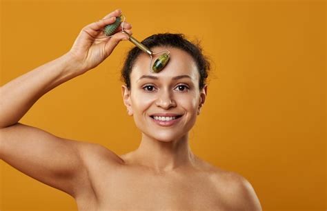 Premium Photo A Beautiful Woman Smiling And Massaging Forehead With Jade Roller Isolated On