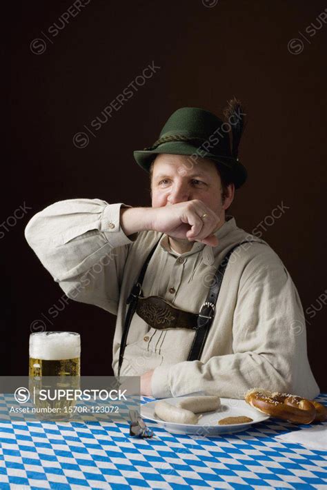 Stereotypical German Man In Bavarian Costume Wiping Mouth At A Table