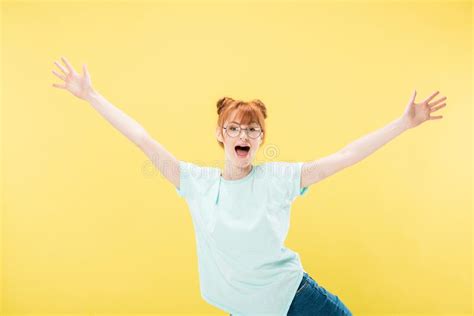 view of excited redhead girl in glasses waving hands and looking at camera isolated on yellow