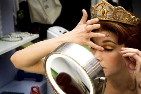 A Woman With A Crown On Her Head Is Looking Into A Mirror And Touching