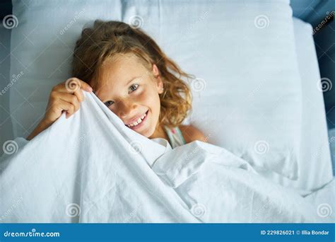 Little Girl Wakes Up From Sleep On A Big And Cozy Bed White Linen In