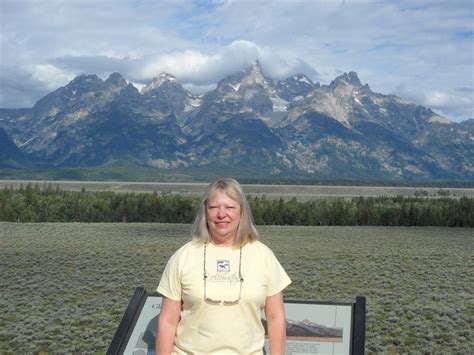 A Woman Standing In Front Of A Sign With Mountains In The Backgrouund