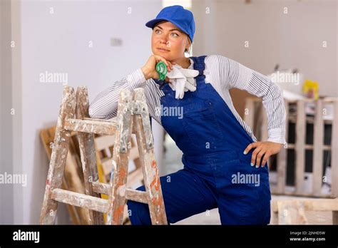 Portrait Of Contented Young Female Builder In Blue Overalls During