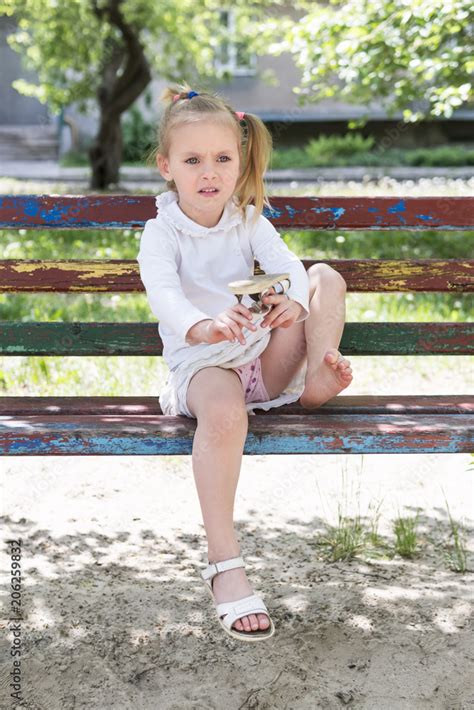 Beautiful Little Girl Sitting On An Old Bench Shakes The Sand Out Of