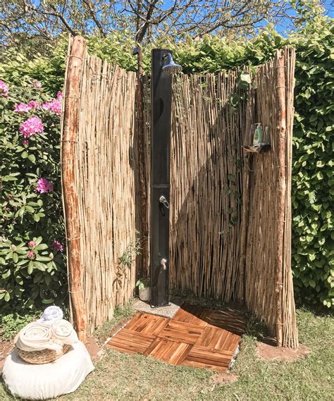 An Outdoor Shower Made Out Of Sticks In The Grass Next To Some Flowers