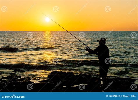 Fisherman At Sunset Throws Tackle Into The Sea Silhouette Of A