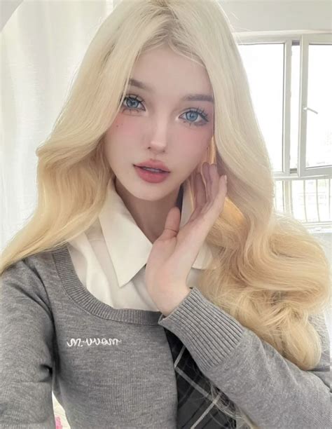 A Blonde Doll With Long Hair Wearing A Gray Sweater And White Collared