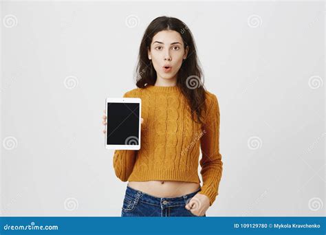 retrato de la mujer atractiva sorprendente que dice guau y que muestra la tableta como si haga
