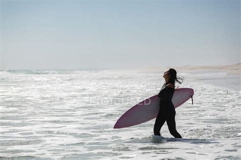 Female Surfer Standing With Surfboard In The Beach On A Sunny Day