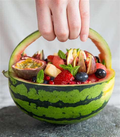 A Person Is Holding A Watermelon Basket Filled With Fruits And