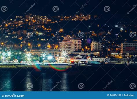 Yalta Embankment At Night City Buildings Lights Reflected In Black Sea