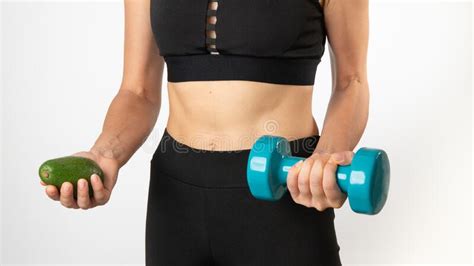 A Woman In Sportswear Holds A Dumbbell And Avocado In Her Hands A