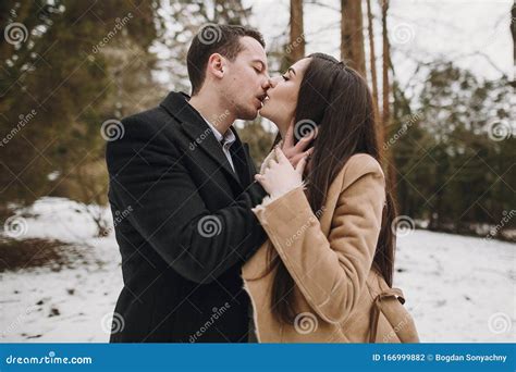 Gorgeous Wedding Couple Kissing In Winter Snowy Park Stylish Bride In Coat And Groom Embracing