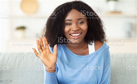 Black Woman Sitting At Home On The Sofa And Waving Stock Photo