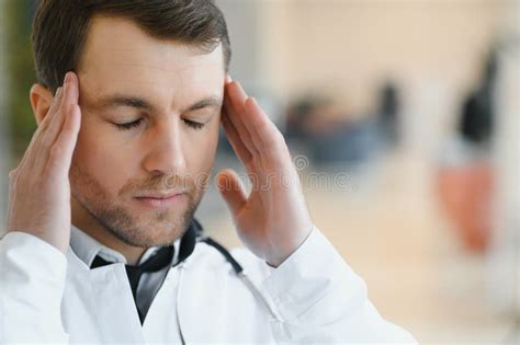 Handsome Young Doctor In White Coat Is Touching His Temples While
