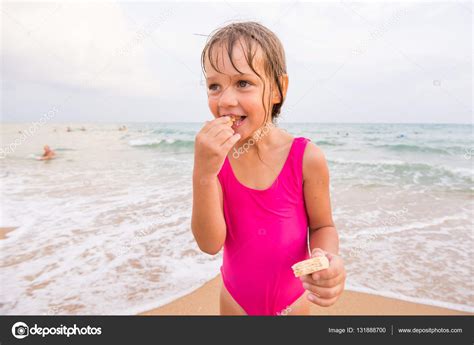 The Girl In The Pink Bathing Suit Standing On The Beach And Eating
