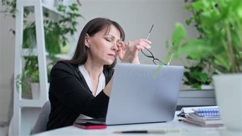 Tired Middle Aged Woman Sitting At Workplace Taking Off Her Glasses Looking Out Window Stock