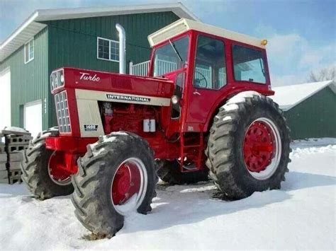 A Red Tractor Parked In The Snow Next To A Green Building With A White Roof