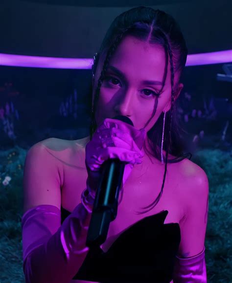 A Woman Holding A Microphone Up To Her Mouth In Front Of A Purple Light And Grass Area