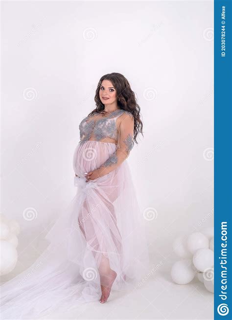 Brunette Pregnant Woman In Transparent Dress Posing In Studio Waiting