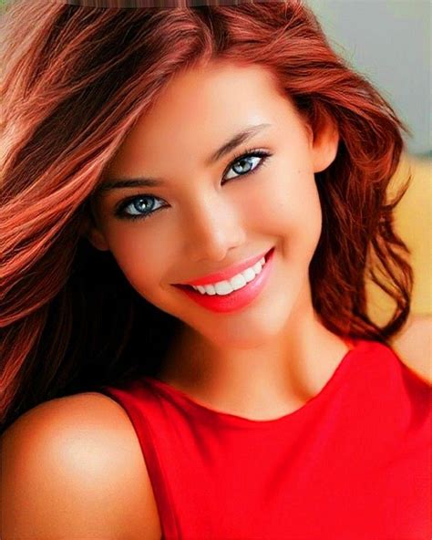 A Woman With Long Red Hair And Blue Eyes Smiling At The Camera While Wearing A Red Top