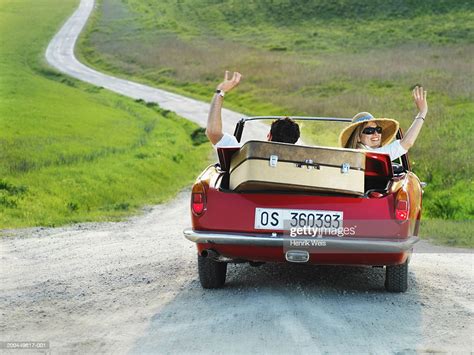 Couple Driving Convertible Car In Countryside Waving Arms Rear View