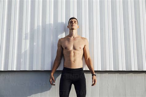 Shirtless Man Standing Against Wall Outdoors Stock Photo