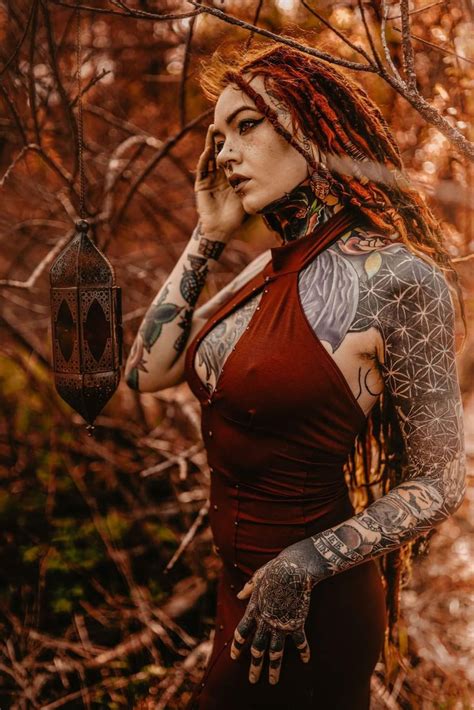 A Woman With Red Hair And Tattoos On Her Arm Holding A Lantern In The Woods