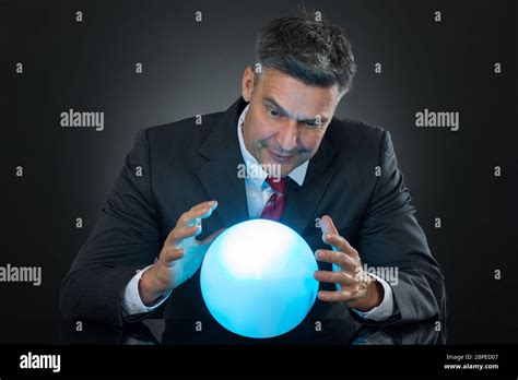 Portrait Of Businessman Predicting Future With Crystal Ball On Desk