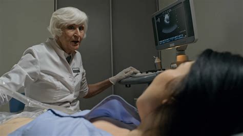 Senior Female Doctor Performing Ultrasound Exam Of Abdomen And Then