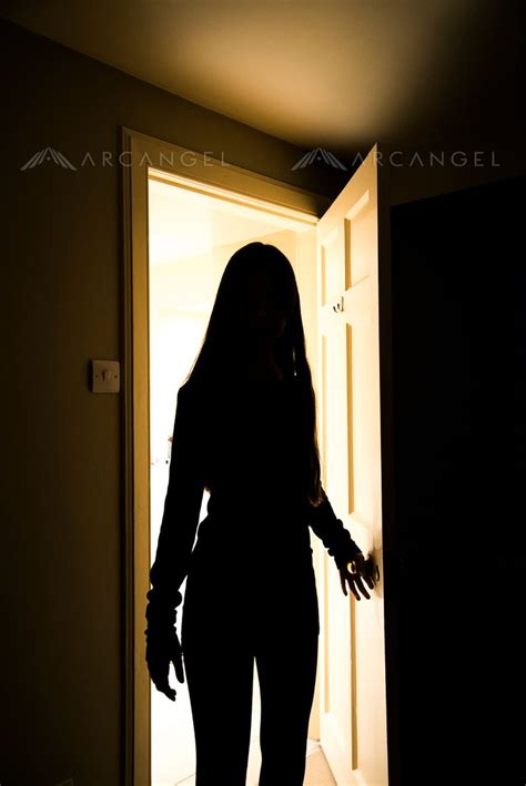an atmospheric image of the silhouette of a woman standing in the doorway into a dark room