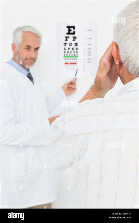 Pediatrician Ophthalmologist With Senior Patient Pointing At Eye Chart