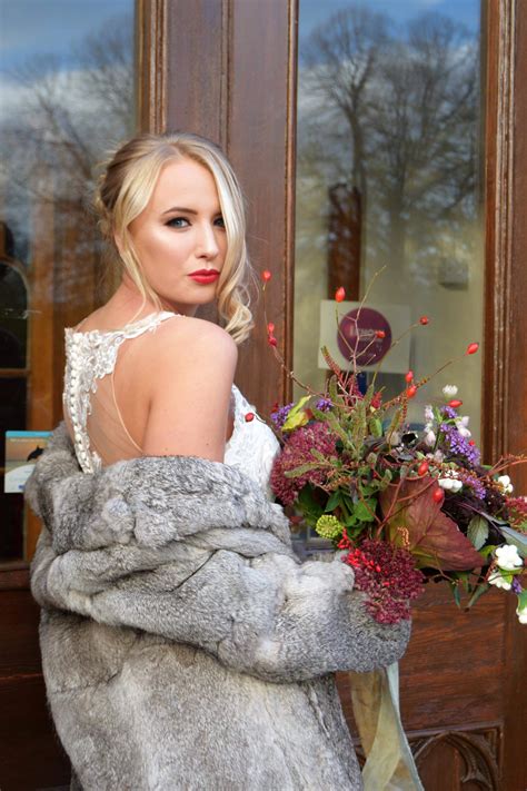 A Woman Wearing A Fur Coat Holding A Bouquet Of Flowers In Front Of A Door