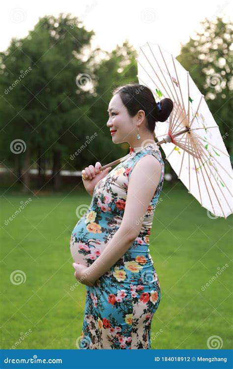 Asian Pregnant Woman In Chinese Traditional Cheongsam Chi Pao Hold Umbrella Parasol In Garden