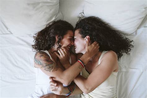 Happy Lesbian Couple Romancing While Lying On Bed At Home Stock Photo
