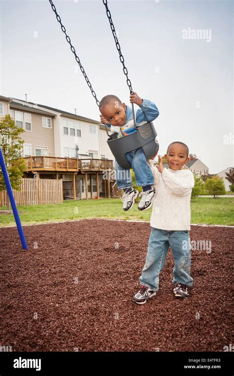 Boy Pushing Younger Brother On Swing Set In Park Maryland Usa Stock