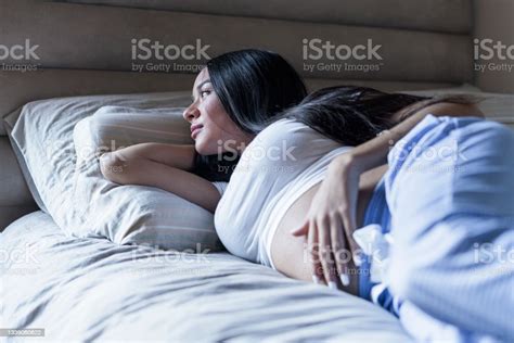Adolescent Woman Lying In Bed In Her Room Touching Her Belly For Her