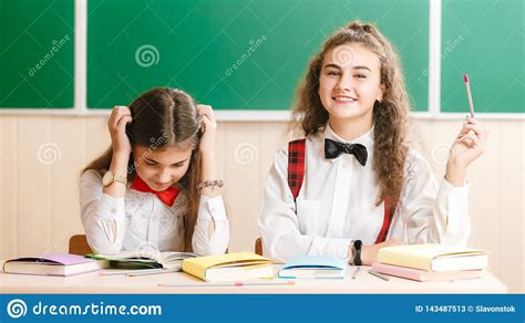 Two Beautiful Schoolgirls Are Sitting At The Desk With Books In The
