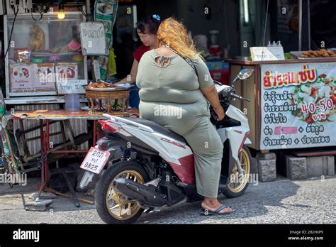 fettleibige frau auf einem motorrad die lebensmittel von einem straßennahrungsmittel stall