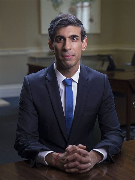 A Man In A Suit And Tie Sitting At A Table With His Hands Folded Out