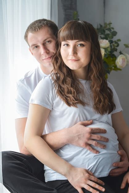 Premium Photo Young Pregnant Woman And Her Husband Are Hugging Touching The Belly Near Window