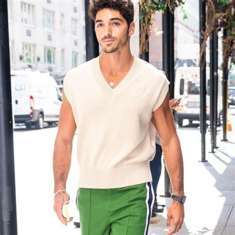 A Man Walking Down The Street Wearing Green Pants And A White Sweater