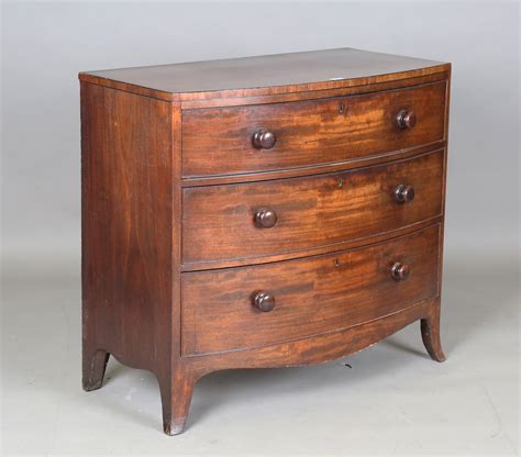 A Regency Mahogany Bowfront Chest Of Three Long Drawers With Turned Bun Handles On Outswept Bracket