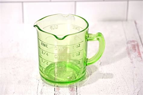 A Green Measuring Cup Sitting On Top Of A Wooden Table Next To A White