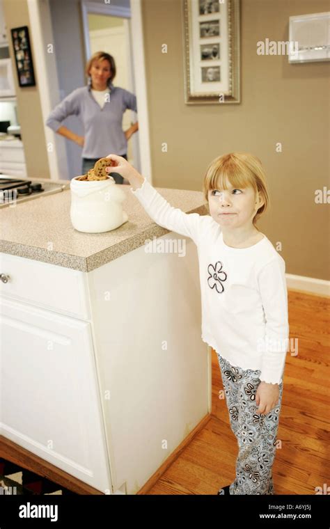 A Mother Watching Her Daughter Take A Cookie From A Jar On The Kitchen