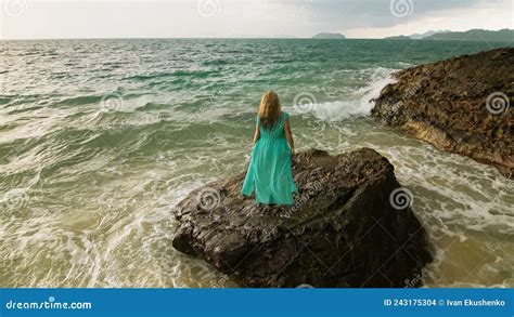 woman walks on rock of sea reef stone stormy cloudy ocean blue swimsuit dress tunic concept